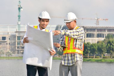 İki Mühendis planlarını elinde tutarak tartışmalı gayrimenkul projesini konuşuyor.
