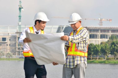 İki Mühendis planlarını elinde tutarak tartışmalı gayrimenkul projesini konuşuyor.
