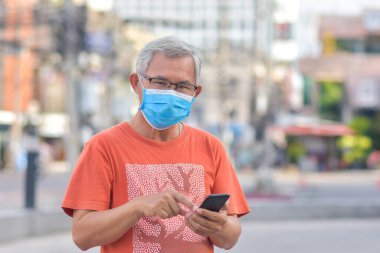 Yaşlı adam tıbbi maske takıyor. Sokak şehrinde cep telefonu tutuyor. Yeni normal maske Coronavirus Covid19 'u koruyor.