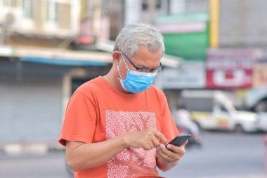 Yaşlı adam tıbbi maske takıyor. Sokak şehrinde cep telefonu tutuyor. Yeni normal maske Coronavirus Covid19 'u koruyor.