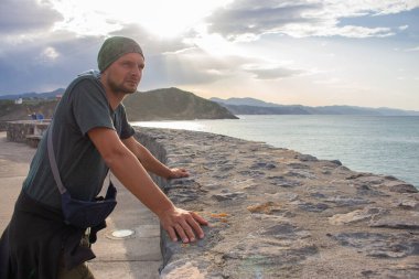 Adam deniz kıyısını dört gözle bekliyor. Deniz kıyısında çırılçıplak duran turist. Dramatik gökyüzü, güneş ışığı ve gezgin manzarası. Aktif yaşam tarzı. Seyahat konseptini hayal et. Boşluk ve özgürlük kavramı.