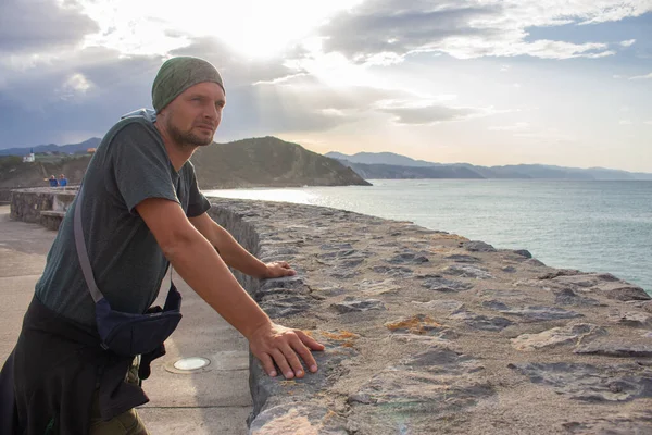 Adam deniz kıyısını dört gözle bekliyor. Deniz kıyısında çırılçıplak duran turist. Dramatik gökyüzü, güneş ışığı ve gezgin manzarası. Aktif yaşam tarzı. Seyahat konseptini hayal et. Boşluk ve özgürlük kavramı.