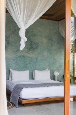 Sivrisinek ağlı ve açık kapısı olan lüks bir otel odası. Tropikal otelin içi rahattır. Rahat ve zarif bir yatak odası tasarımı. Tropik bölgelerde yaz seyahati. Turist beldesi. Baldachin 'le yatak. Modern ev tarzı.