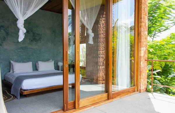 Luxury hotel room with mosquito net and open terrace. Comfortable interior of tropical hotel. Cozy and elegant bedroom design. Summer travel in tropics. Tourist resort. Bed with baldachin. Modern home style.