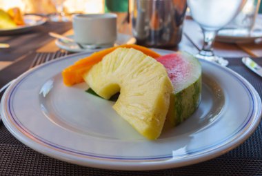 Açık hava restoranında bir tabak sulu meyve. Otel kahvaltısı. Kahvaltı masası servisi. Bir dilim ananas, karpuz ve tabakta papaya. Lezzetli tatlı. Masada taze meyve var. Meyve ve kahve..