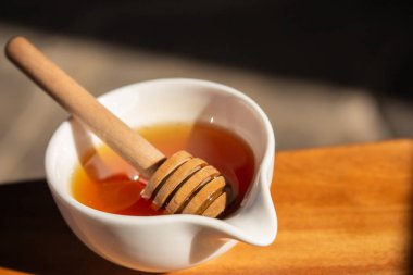 Bal ve küçük beyaz kâse. Güneş ışığında ahşap çubuklu ev yapımı bal. Kavanozda bal. Doğal tatlandırıcı. Sağlıklı beslenme. Doğal tatlı konsepti. Tatlı yemek..