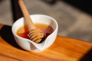 Bal ve küçük beyaz kâse. Güneş ışığında ahşap çubuklu ev yapımı bal. Kavanozda bal. Doğal tatlandırıcı. Sağlıklı beslenme. Doğal tatlı konsepti. Tatlı yemek..