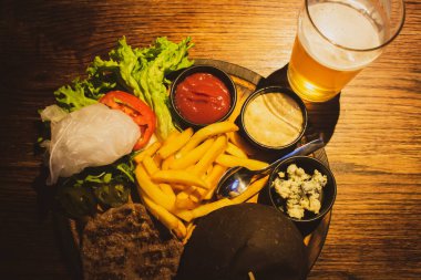 Burger ingredients with beer glass on the table, top view. Hamburger, sauce, fried potato and beer. Pub menu. Fastfood concept. Served plate of meat and potato. Takeaway meal. Self made meal. 