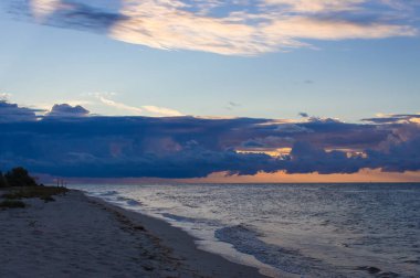 Denizin üzerinde gün doğumu manzarası. Kumsalda sabah alacakaranlığı. Bulutlu dramatik sabah gökyüzü. Alacakaranlıkta yaz deniz manzarası. Sakin denizi ve huzurlu gündoğumu olan boş bir sahil şeridi. Bulutların arasından geçen altın güneş.