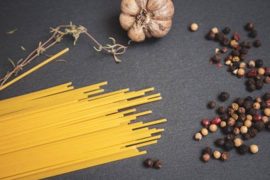 Çiğ spagetti, sarımsak ve kartonda biber karışımı. Baharatlı ve sarımsaklı çiğ makarna. İtalyan mutfağı tarifi. Sağlıklı yiyecekler. Yemek pişirme konsepti. Ev yapımı yemekler. Yemek malzemeleri siyah masada..