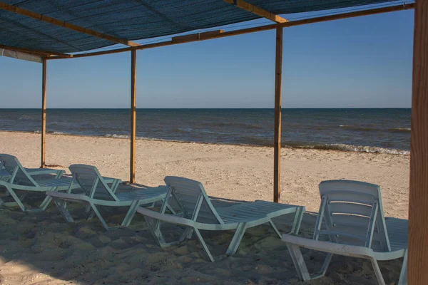 Lounge chairs on the beach. Empty resort on Black Sea. Sun beds under cover on the coast. Idyllic place for summer relaxation. Lounge chairs on seascape background. Vacations on island. Row of empty beach chairs. Summer travel concept.