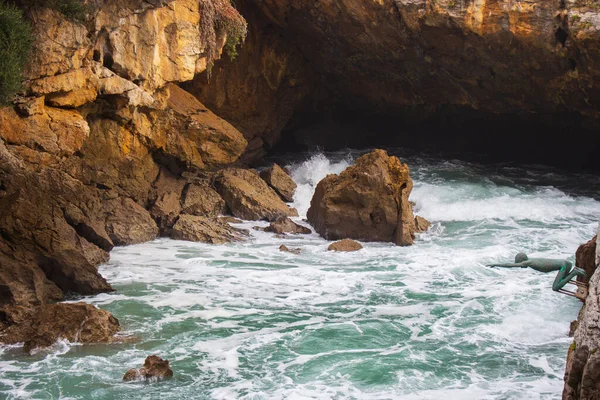 Castro Urdiales, İspanya - 10.19.2019: Akşam güneşinde deniz kenarında küçük bir heykel. Atlantik Okyanusu kıyısındaki kayalık mağarada. Kıyı doğası. Gün batımında Cantabria manzarası. Biscay Körfezi 'nin inanılmaz dalgaları kayalarda.