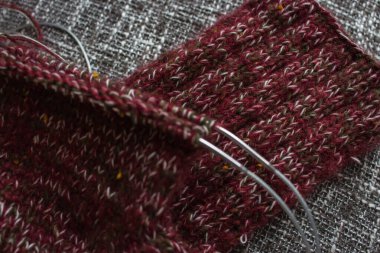 Gri arka planda iğnelerin üzerine örülmüş çoraplar. Örgü iğnelerinde kırmızı, yeşil ve beyaz ipliklerin karışımı. Yün çorap örme işlemi. Örgü hobisi. Örgü giyme konsepti. Örgü işi geçmişi. Çoraplar için örgü deseni.