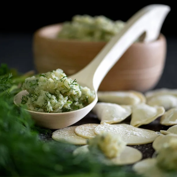Homemade Dumplings, lean food, Cooking process. Dill potatoes filling and rolling Raw dough circles sprinkled with flour. Ingredients on large wooden spoon. Preparation of Convenience Food. Close up
