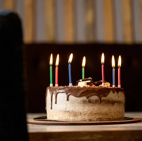 Karanlık arka planda doğum günü pastası. Çikolata kremalı, bayramlık tatlının üstünde yedi mum yanıyor. Sevdiğin kişi için şeker ya da tatil etkinliği. Bayram kartı ya da bayram afişi için boş. Boşluğu kopyala