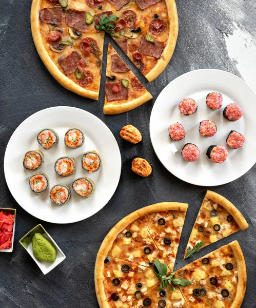 Sushi rolls and pizza set on black table background. High angle view