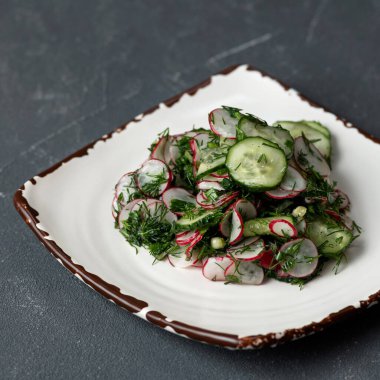 Doğal vitamin ürünü. Kil tabağında salatalık, turp ve dereotu karıştırılmış. Taze sebze ve yeşil eko salata. Yiyeceğin parlak rengi. Yumuşak odaklanma, kare format. Üst görünüm