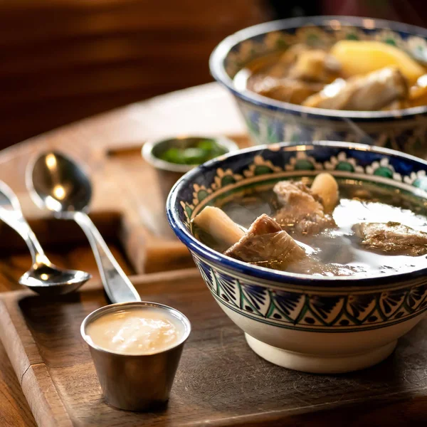Bowls with Rich hearty meat soup with broth and pork ribs on wooden table. Nutritious wholesome food. Delicious hot lunch or dinner. Close up shot. Soft focus