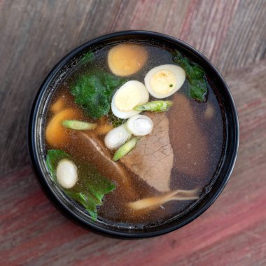 Et çorbası ve yumurtalı erişteli Japon eriştesi çorbası. Tahta bir masada bir kase doyurucu yemek. Baharatlı doğu yemeği, Pan-Asya mutfağı.