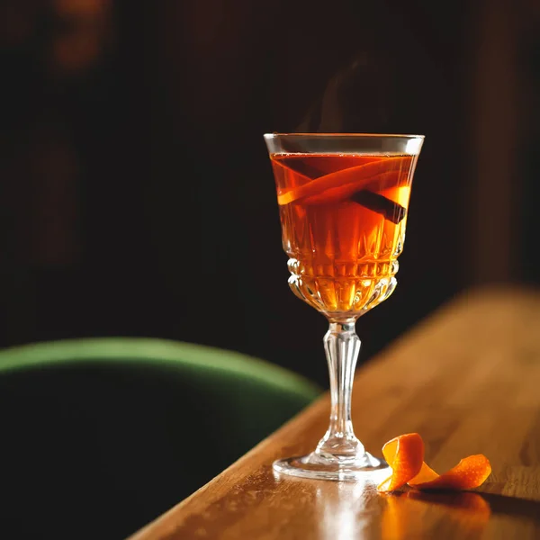 Склянка з коктейлем на дерев'яному столі на фоні чорного фону. Міцний алкогольний напій з паличкою кориці та шматочком апельсина. М'який фокус. Копіювати простір для тексту — стокове фото