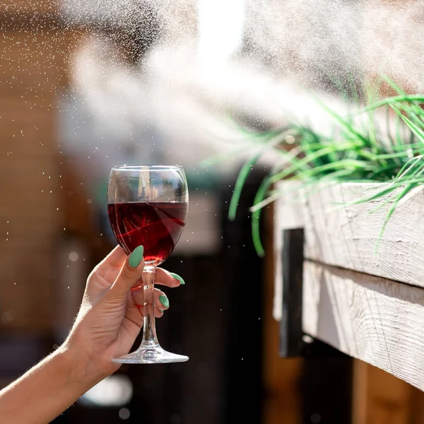 Женская рука держит стакан с красным вином на размытом фоне с брызгами воды. Алкогольные напитки — стоковое фото