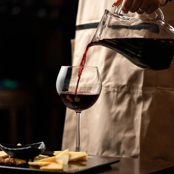 Сомелье наливает красное вино из стеклянного кувшина в бокал вина на черном фоне. Крупный план. Алкогольные напитки и напитки — стоковое фото