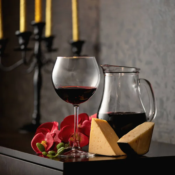 Стеклянный кувшин и бокал вина с красным вином, красные цветы орхидеи и сыр на винтажном фоне подсвечника. Алкогольные напитки — стоковое фото