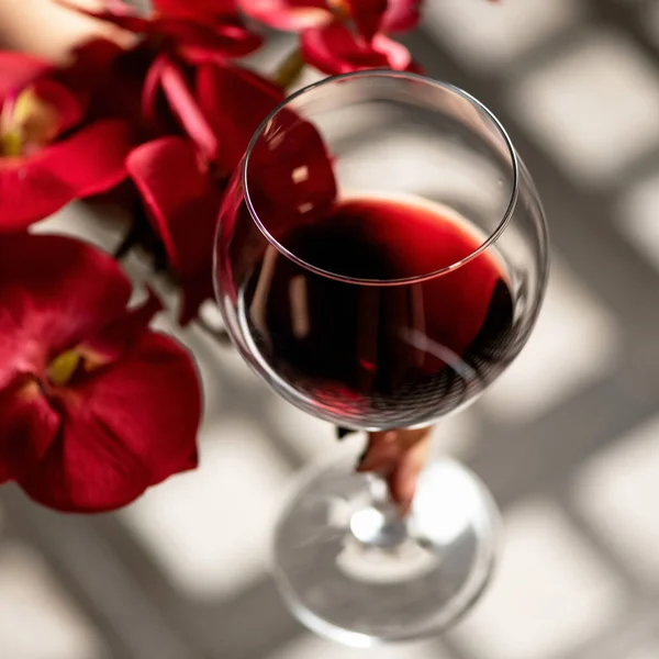 Стакан красного вина и цветы красной орхидеи на деревянном столе с блеском солнца. Алкогольный напиток. Крупный план, мягкий фокус — стоковое фото