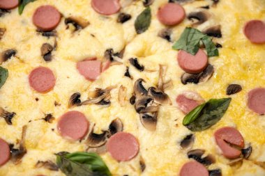 Eritilmiş peynirli, mantarlı, sosisli, yeşil fesleğenli lezzetli bir pizza. Geleneksel İtalyan yemekleri. Abur cubur. Yakın çekim, yumuşak odaklanma. Yatay biçim