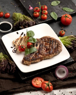 Siyah ahşap masada servis edilen beyaz tabakta nefis ızgara et. Restoranda öğle yemeği. Dikey format. Sebzeli sulu biftek.
