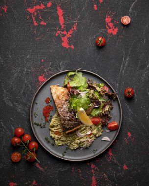 Sebzeli kızarmış somon fileto. Deniz ürünleri konsepti. Siyah arka planda pişmiş kırmızı balık, limon, domates ve yeşillik tabağı. Lokantada güzel servis tabağı. Üst Manzara. Kare format veya 1x1. Anlaşıldı.