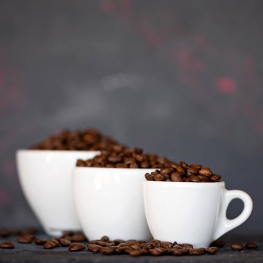 Beyaz bardaklarda kavrulmuş kahve çekirdekleri, en küçüklerden en büyüğe kadar, gri arka planda bulanık arkaplanda, görüntünün üstünde de fotokopi alanı var. Yakın çekim, yan görüş. Yumuşak odak