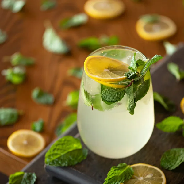 Glass with refreshing vitamin lemonade on wooden table. Soft drink with citrus or lemon slices and mint leaves. Close up shot. Soft focus. Healthy fresh drink. Bright colors of nature. Copy space — Foto de Stock
