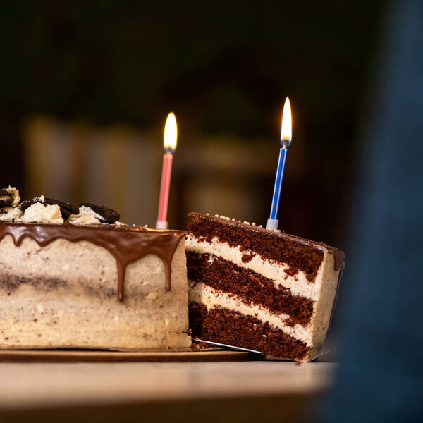 Birthday cake on dark background. Two burning candles on top of festive dessert with chocolate icing. Sweets for loved one or holiday event. Blank for greeting card. Copy space. Close up shot