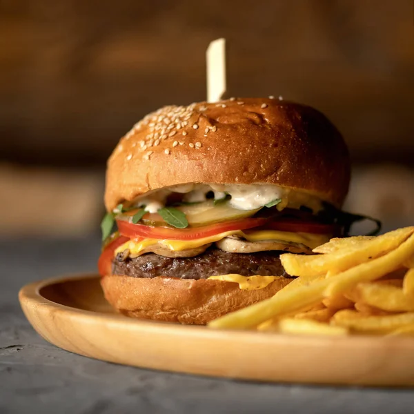 Menú clásico de comida rápida americana. Primer plano de papas fritas y hamburguesa grande con queso sobre fondo borroso. Placa de comida chatarra. Aperitivo, cena o almuerzo. Formato cuadrado — Foto de Stock