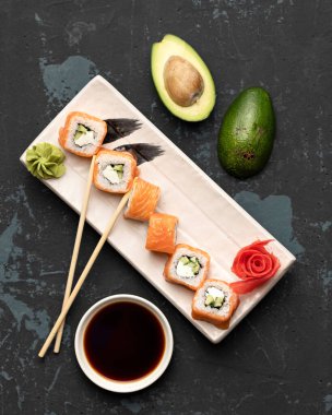Siyah arka planda Suşi seti. Philadelphia somon ve avokado ile birlikte yenmeye hazır. Turşulu zencefil, wasabi ve soya sosuyla süslenmiş sağlıklı Japon yemekleri. Üst Manzara. Refah kavramı