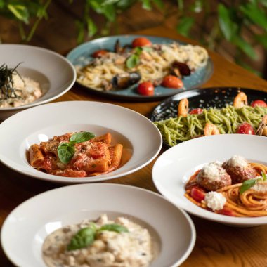 Restoran masasında hamurdan pişirilmiş yemekler. Erişte tabakları, spagetti ve farklı soslu makarna. Şenlik masasında bolca lezzetli yemek var. Yumuşak odak