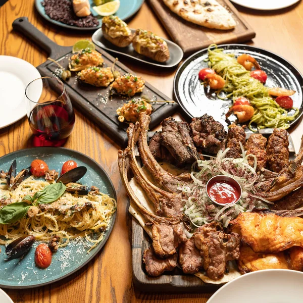 Kırmızı şarap, ızgara et ve ahşap arka planda yeşiller. Şenlik masasında bolca lezzetli yemek var. Kare biçiminde. Üst görünüm