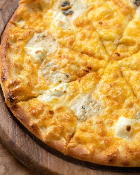 Fırınlanmış peynirli pizza. Eritilmiş parmesanlı ve ahşap tahtada mozzarella soslu Kesik Pizza 'nın yakın çekimi. Dikey format, vejetaryen yemekleri. Yumuşak odak
