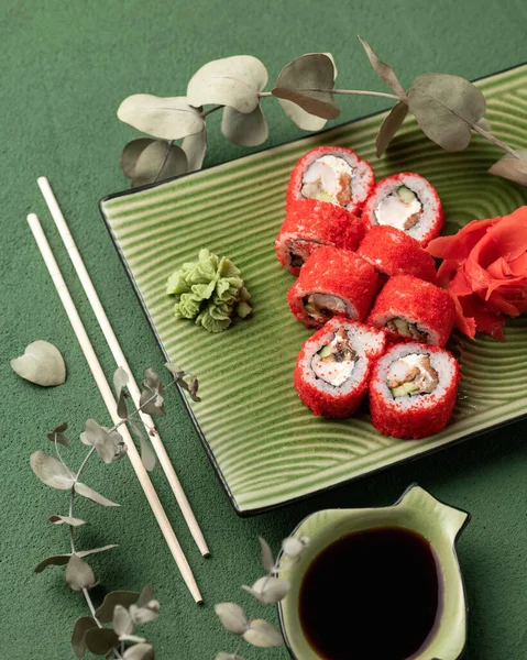 Flat lay. Red Sushi roll in masago or tobiko caviar. Inside-out Sushi Set on green background. Bright colors. Classic Japanese food. Healthy Oriental meall. Top view. Soft focus. Vertical format