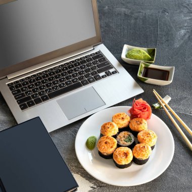 Japon dürümleri, iş, suşi molası. Boş ekranlı dizüstü bilgisayar, günlük, fırında pişmiş suşi rulosu, soslar ve yemek çubukları. Sağlıklı doğu yemekleri. Üst taraf manzarası. Yumuşak odak