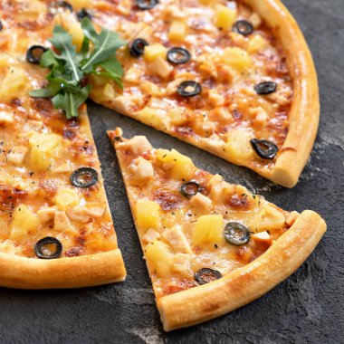 Ananaslı ve zeytinli pizza. Yakın plan çekimde dilimlenmiş pizza ve büyük dilim siyah arka planda. Vejetaryen ya da vejetaryen yemeği. İtalyan abur cubur teslimatı. Yumuşak odak