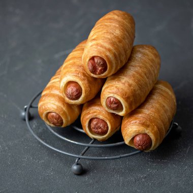 Gri arka planda sosisli sandviç piramidi, yakın plan. Taze pişmiş yiyecekler, poğaça sosisi. Abur cubur konsepti. Uzayı kopyala Kare biçiminde. Yumuşak odak