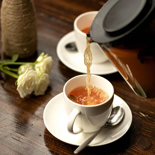 Schwarzer Tee aus klarer Teekanne in Teetasse und Rosenstrauß auf Holztisch. Romantisches Date. Tee für zwei. Nahaufnahme. Weicher Fokus — Stockfoto