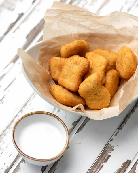 Trozos fritos de queso o carne empanados en papel pergamino con salsa de leche. Snack ligero. Cuenco de sabrosa comida en la mesa rústica blanca. Enfoque suave —  Fotos de Stock