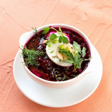 Yeşillik ve yumurtalı soğuk çorba. Beyaz kase kırmızı pancar çorbası, pembe arka planda otlar, üst manzara. Dereotlu, maydanozlu ve yarım yumurtalı vitamin yemeği. Yumuşak odaklanma. Boşluğu kopyala