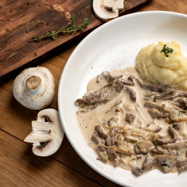 Ekşi krema soslu mantarlı öğle yemeği. Bir tabak patates püresi ve rustik ahşap masa üzerinde şampiyon jülyen. Üst görünüm