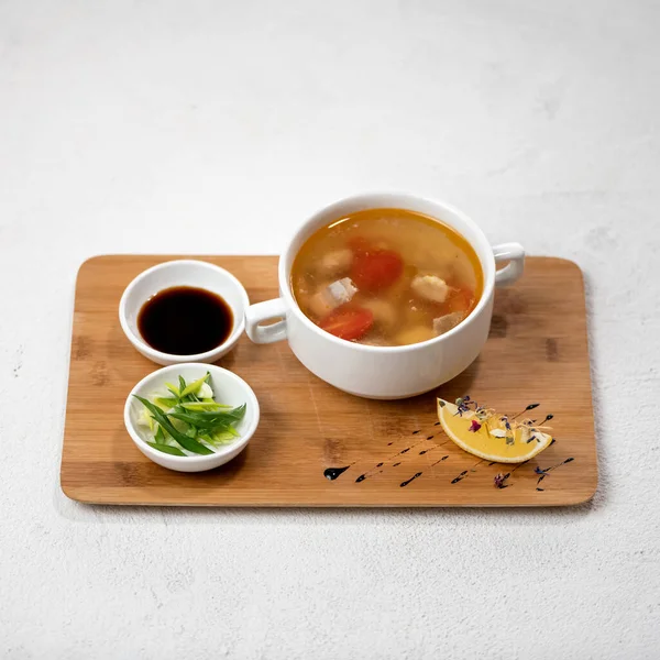 Poultry meat soup with tomatoes and lemon, soy sauce and chopped onions on wooden cutting board. Beautiful serving of food. Object isolated on white background — Stock Photo, Image