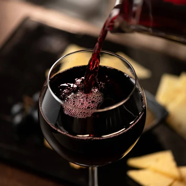 Дорогое красное вино, наливаемое в бокал. Винное стекло с мерло или совиньон на размытом фоне. Крупный план. Роскошный алкогольный напиток или напитки — стоковое фото