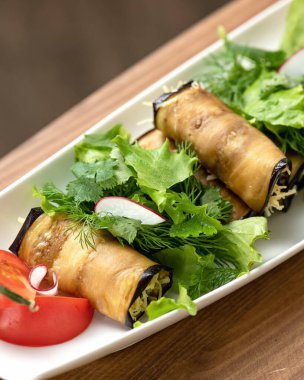 Patlıcan Rolls. Sebzeli aperatif. Doldurulmuş patlıcan dilimleri tabakta domates ve maydanozla. Dikey format. Yumuşak odak